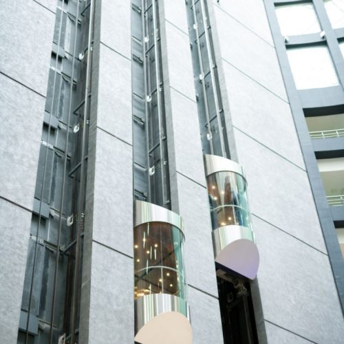 Tall modern office hall with moving glassy elevators, urban business center